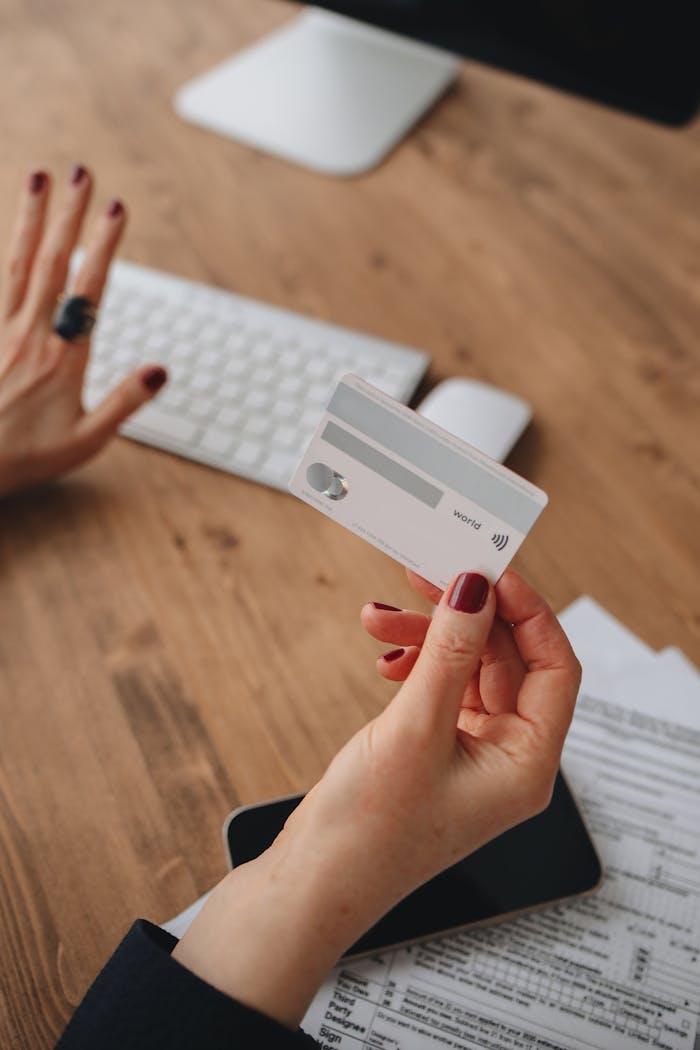 Close-up shot of a person holding a credit card near a keyboard on a wooden table, demonstrating online payment concept.